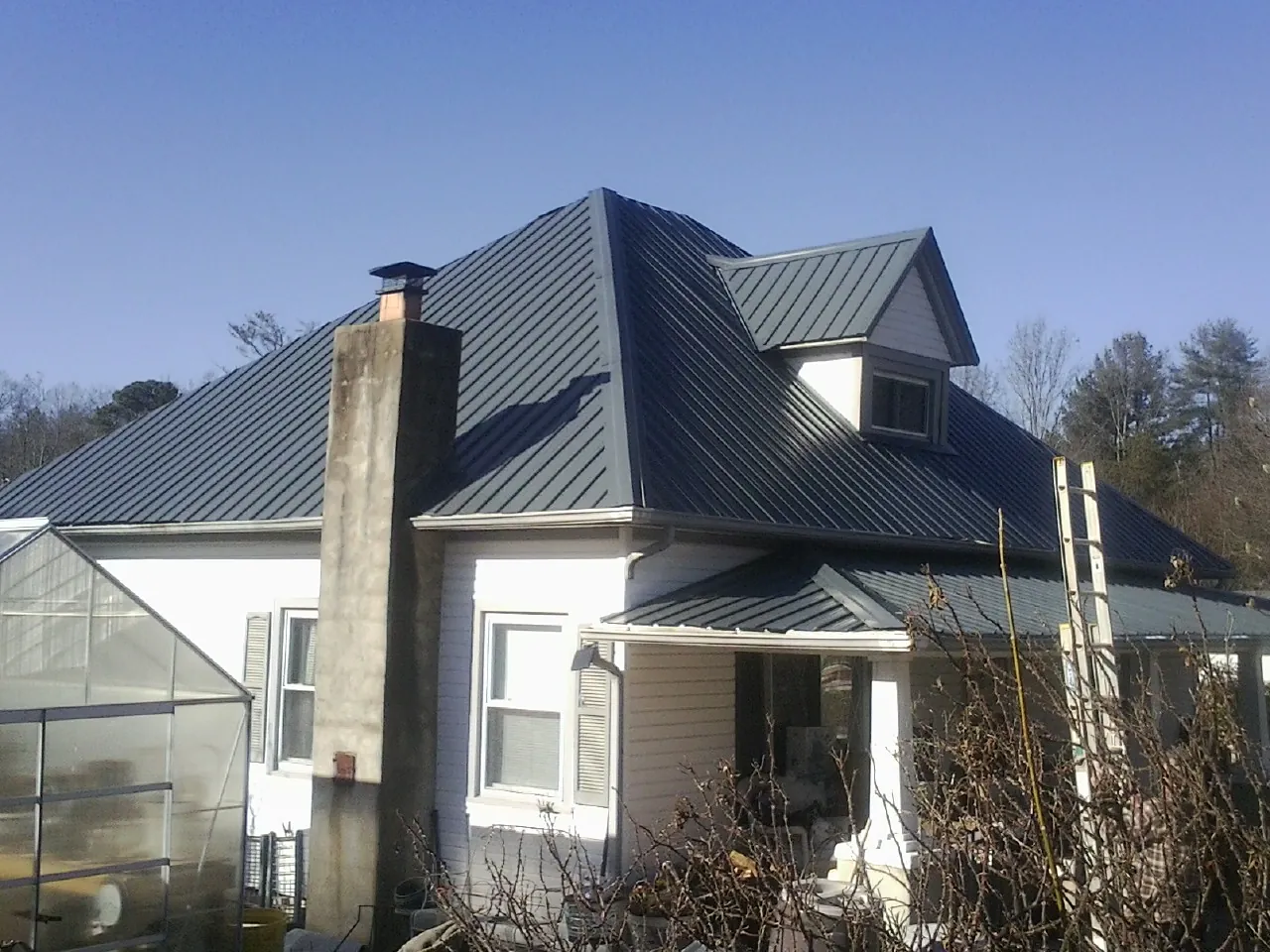 Dark blue standing seam metal roof on a white farmhouse with dormer — Slate & Tile Roof Repair by Roofing Brothers in Pomona